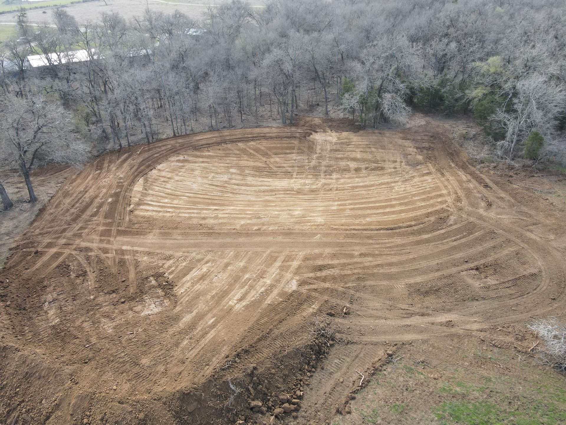 Cleared area in a field surrounded by bare trees, marked with tire tracks, ready for construction.