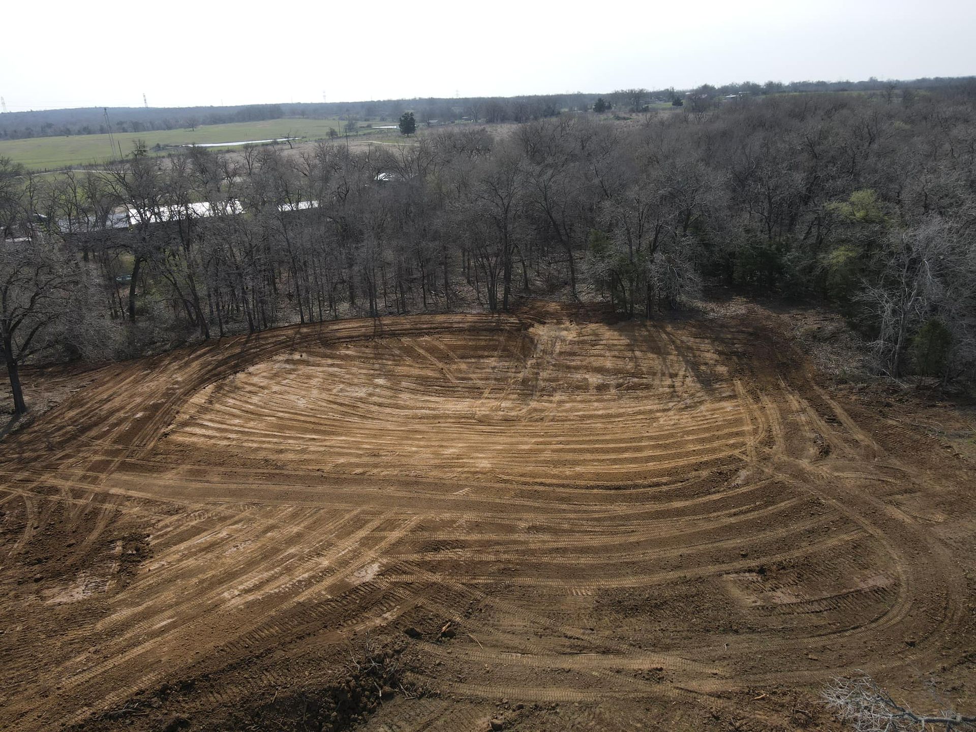 Cleared dirt land surrounded by bare trees, possibly for construction, in a rural setting.