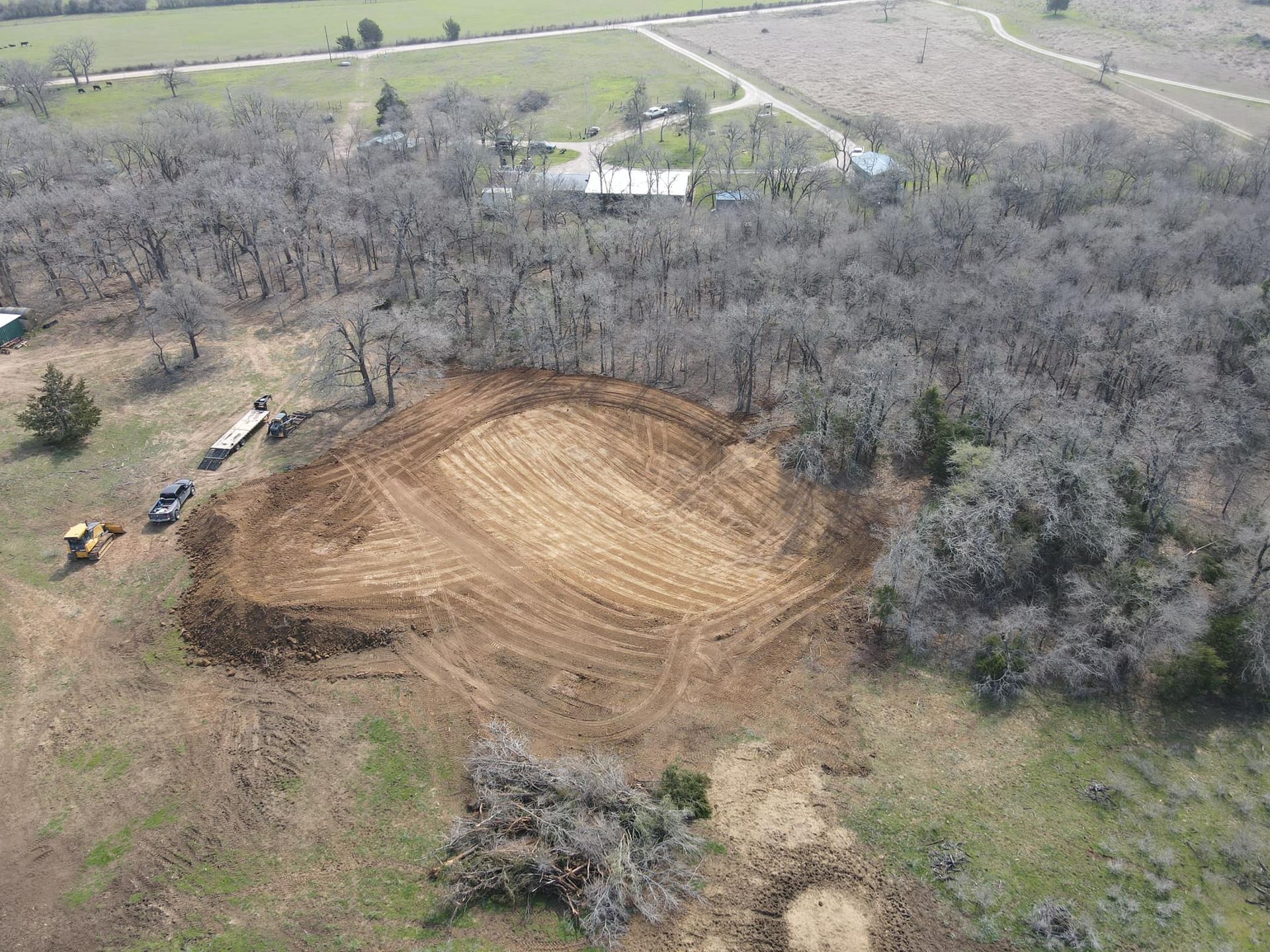 Aerial view of land clearing. Trees surround a large cleared oval, near buildings and fields.