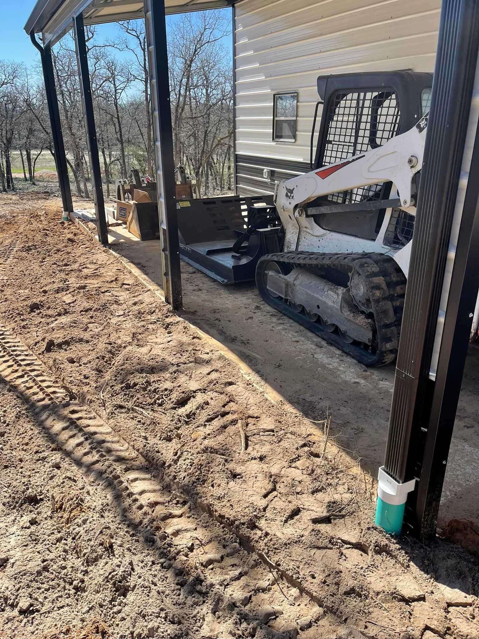 A Bobcat tracked skid steer mower parked near a covered structure on a sunny day.