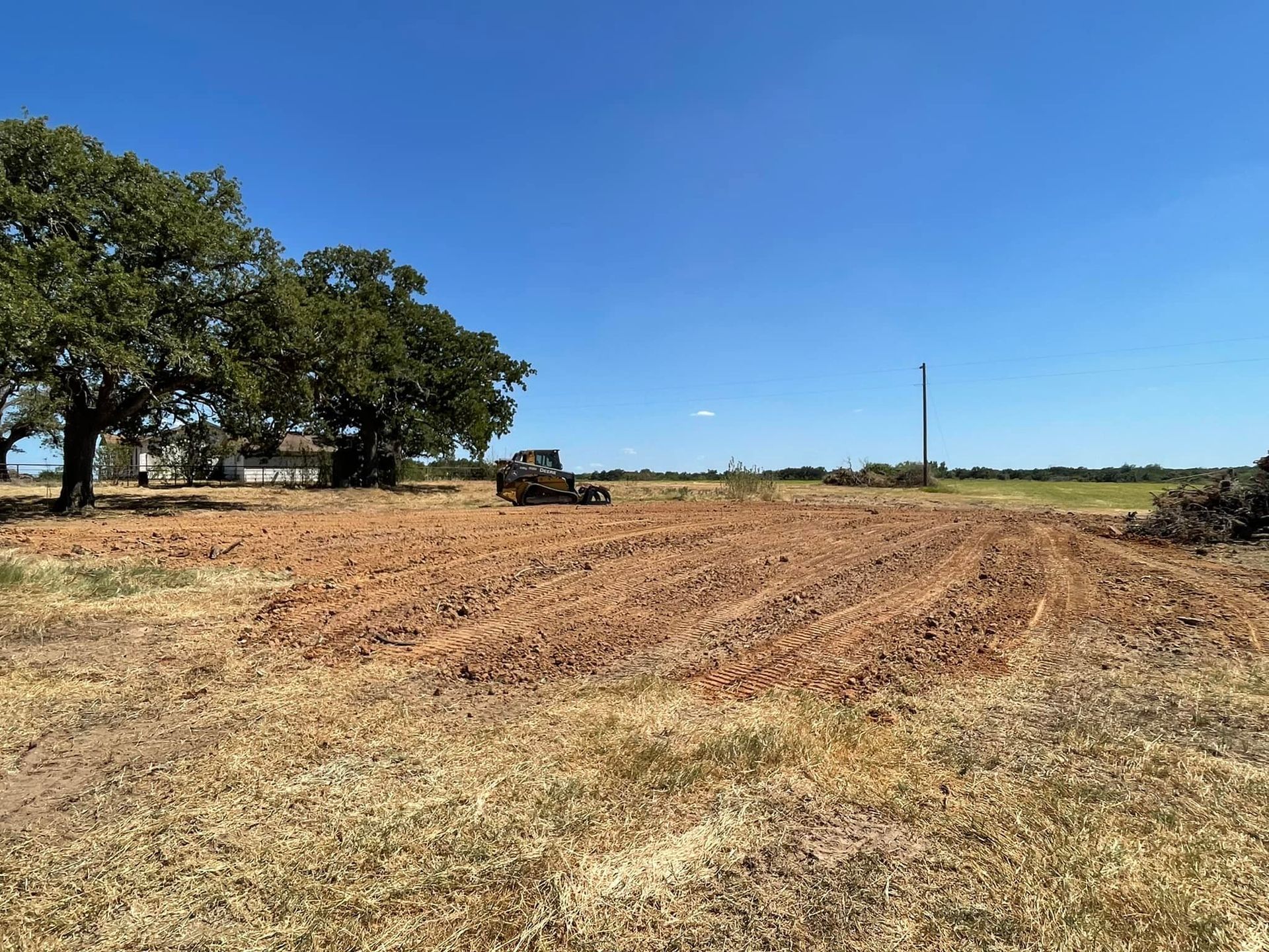 A tractor on a field of plowed brown earth under a bright blue sky.