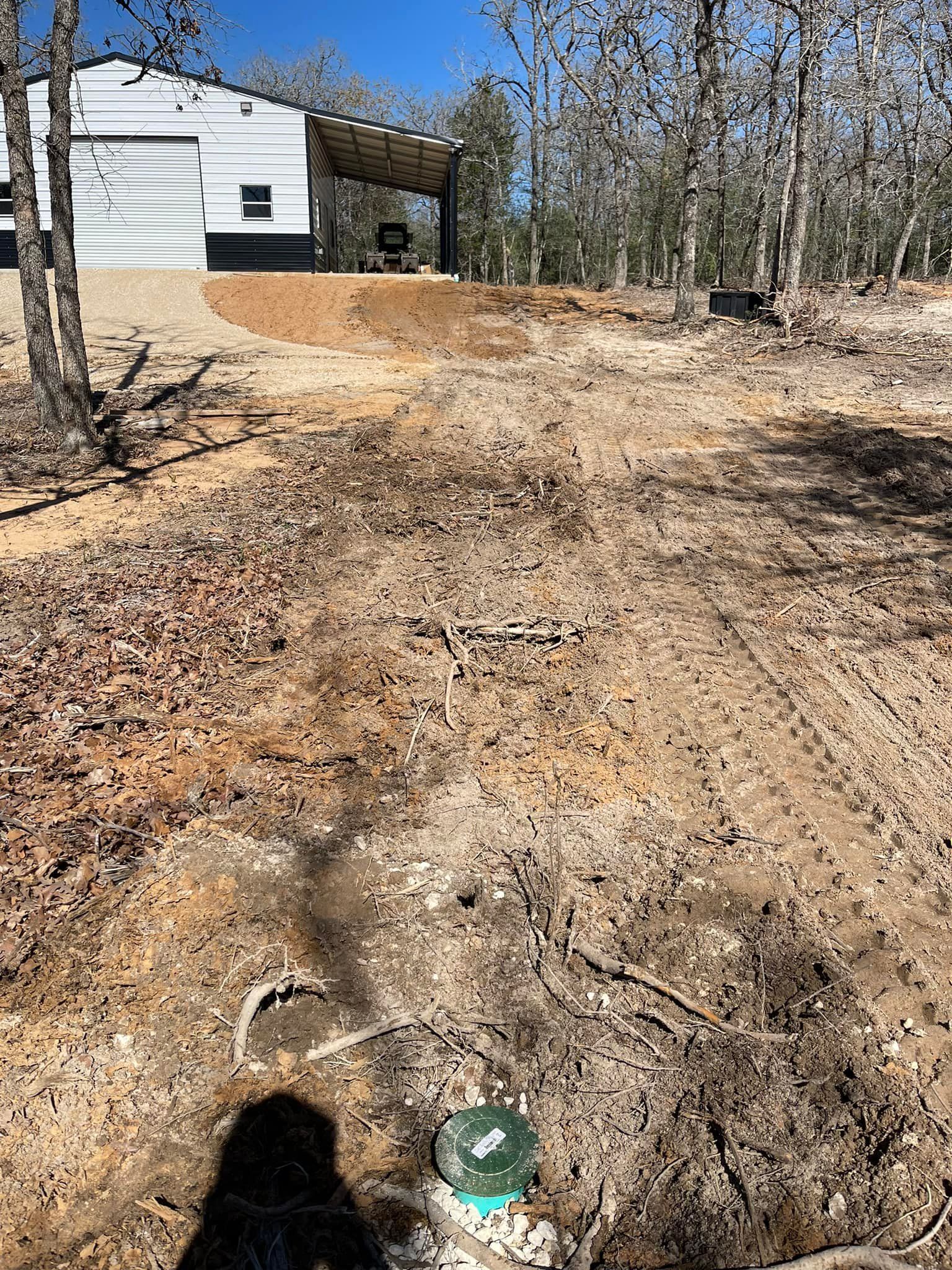 Dirt path leads toward a building with a covered patio. Sunlit, outdoor setting.
