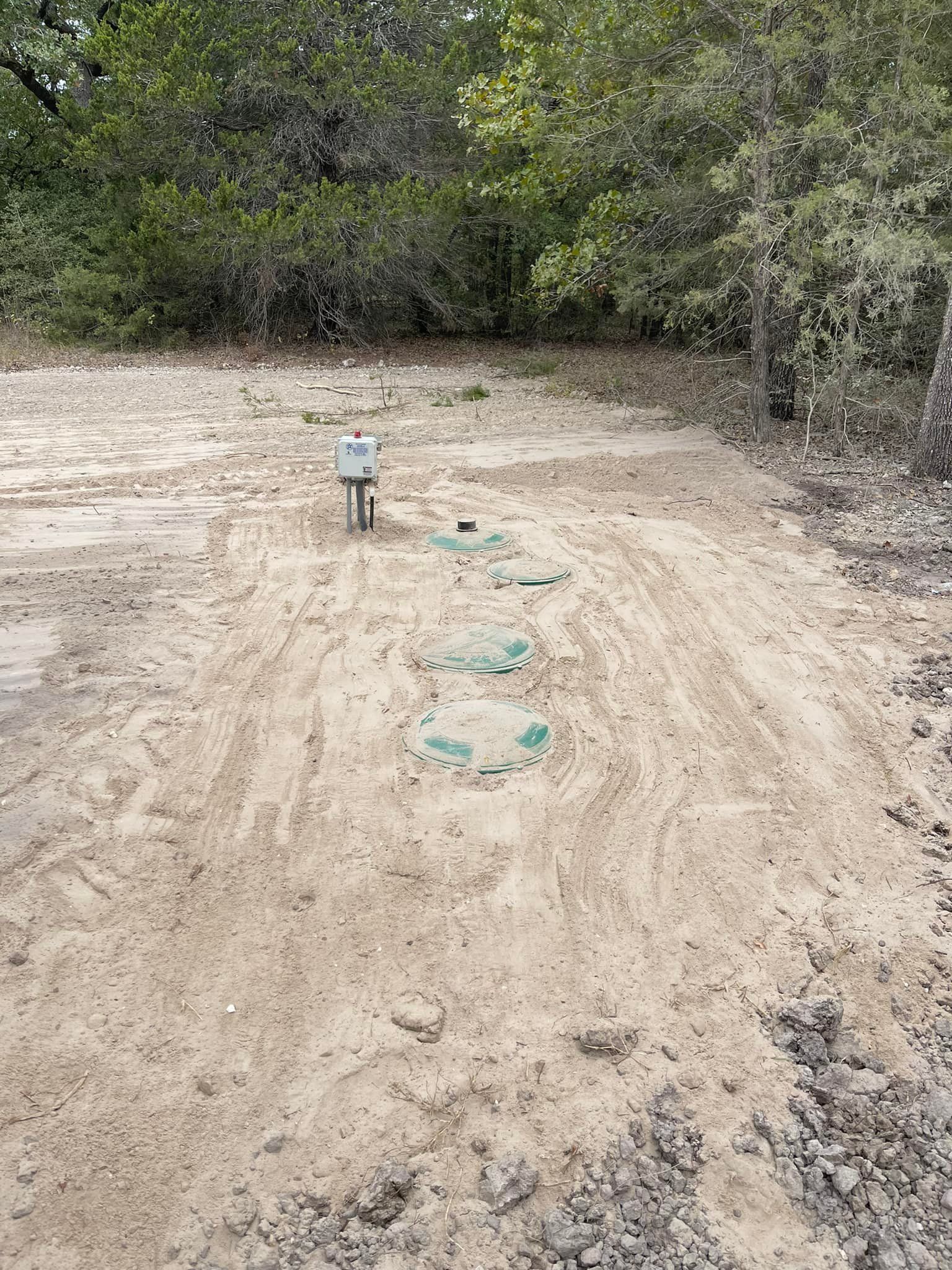 Sandy area with a control box and several green inspection ports, trees in background.