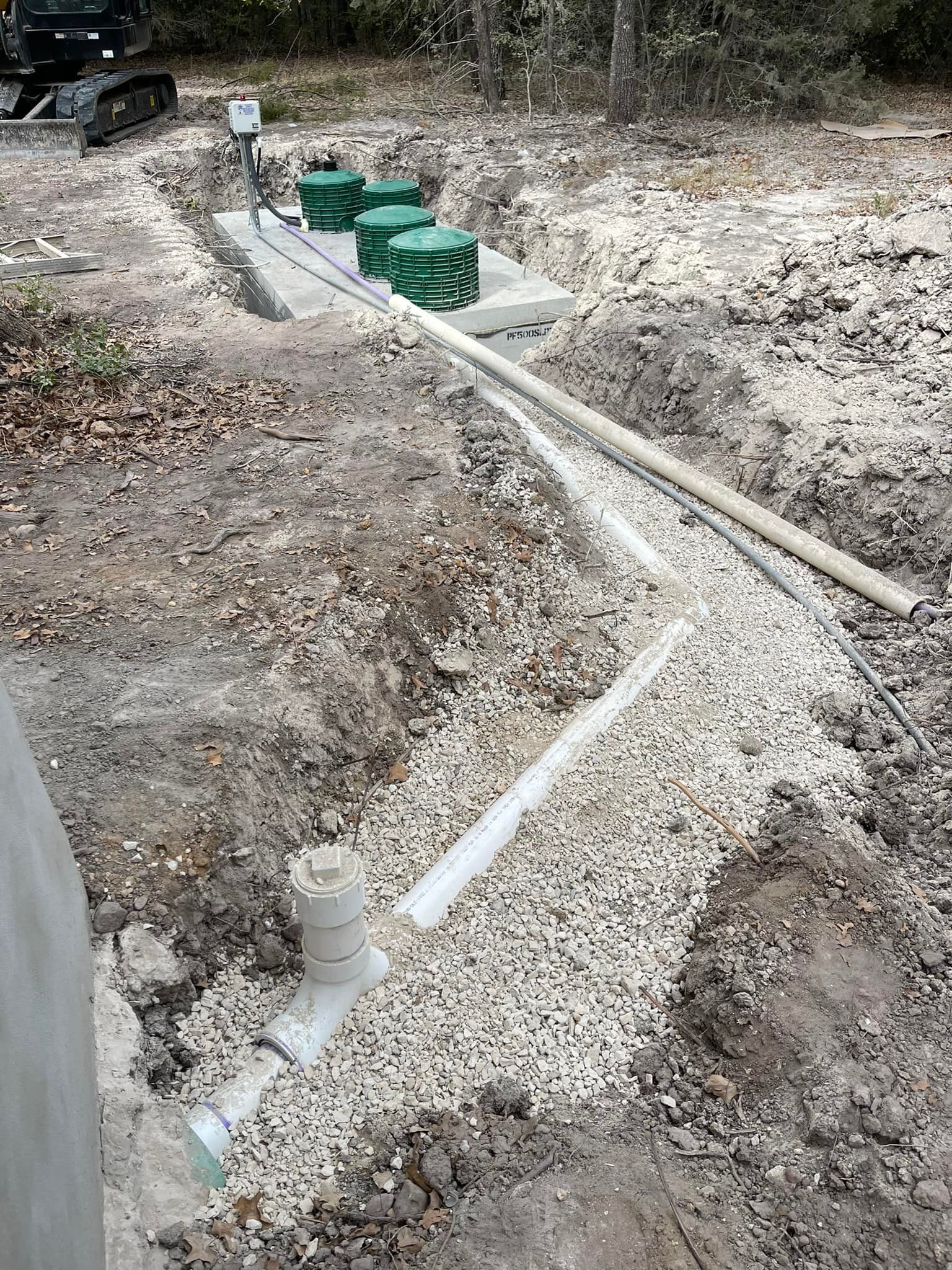A septic system installation in progress outdoors with gravel, pipes, and tanks.