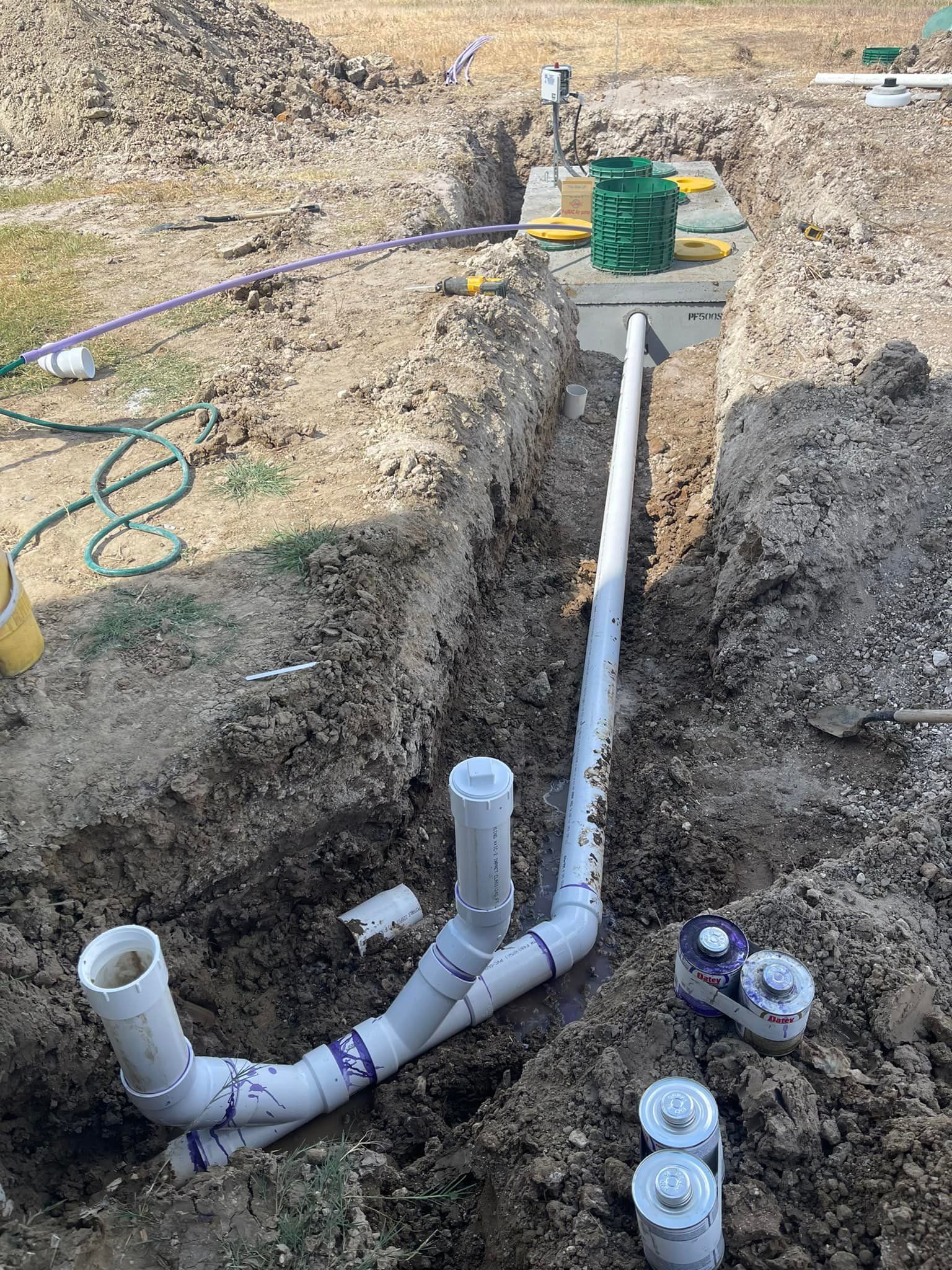 Construction of a septic system, showing trenches, pipes, a tank, and other components in a dirt setting.