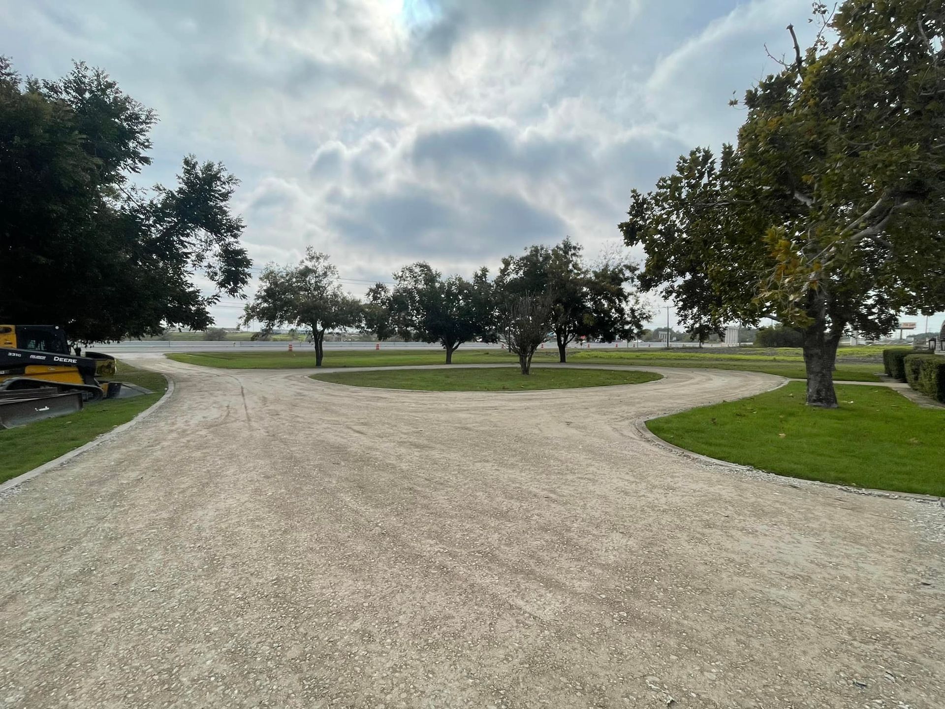 Gravel drive splits into three paths, trees on a grassy island, overcast sky.