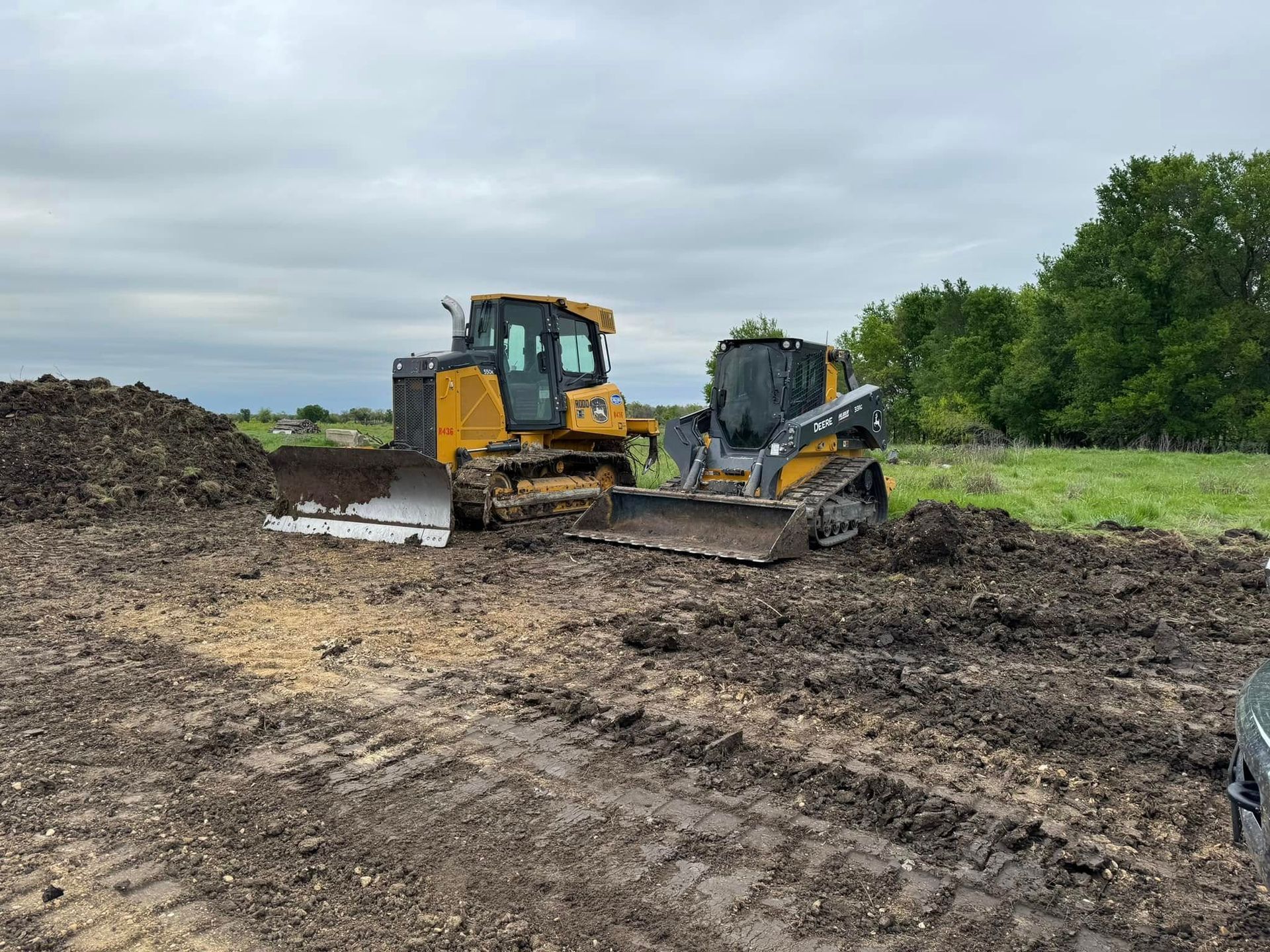 Two yellow construction vehicles on muddy ground; overcast sky.