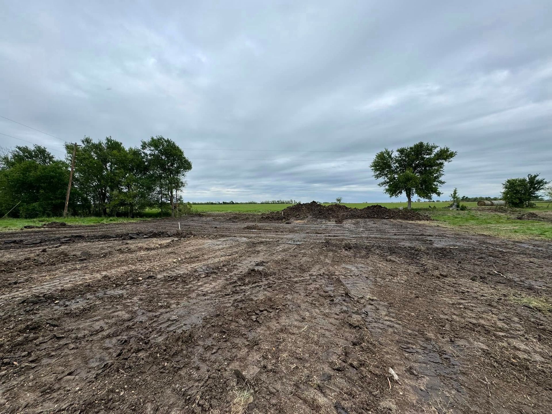 Muddy field with tire tracks, trees in the background, and a cloudy sky.