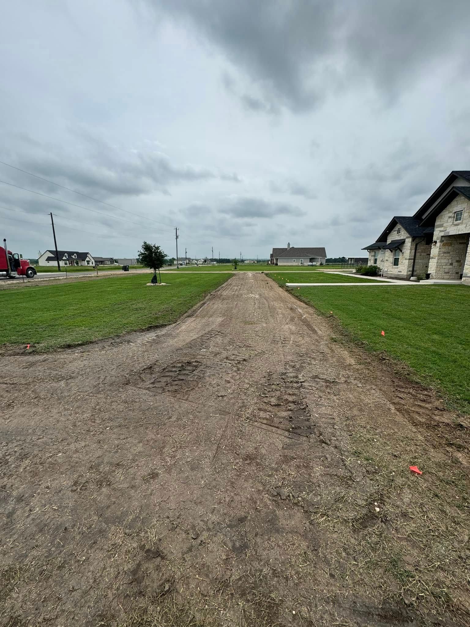 Gravel path in a grassy area leading to houses under a cloudy sky.