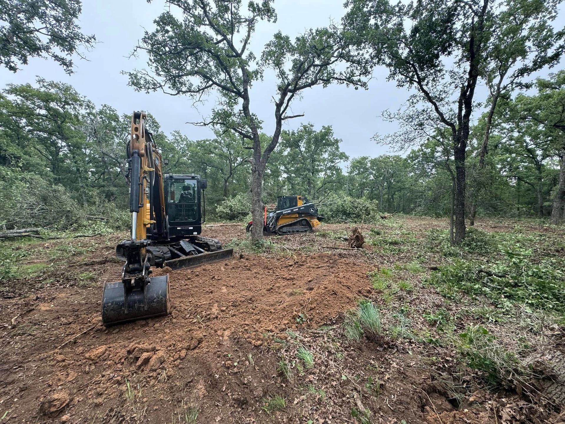 An excavator and a skid steer clearing a wooded area of brush and trees.