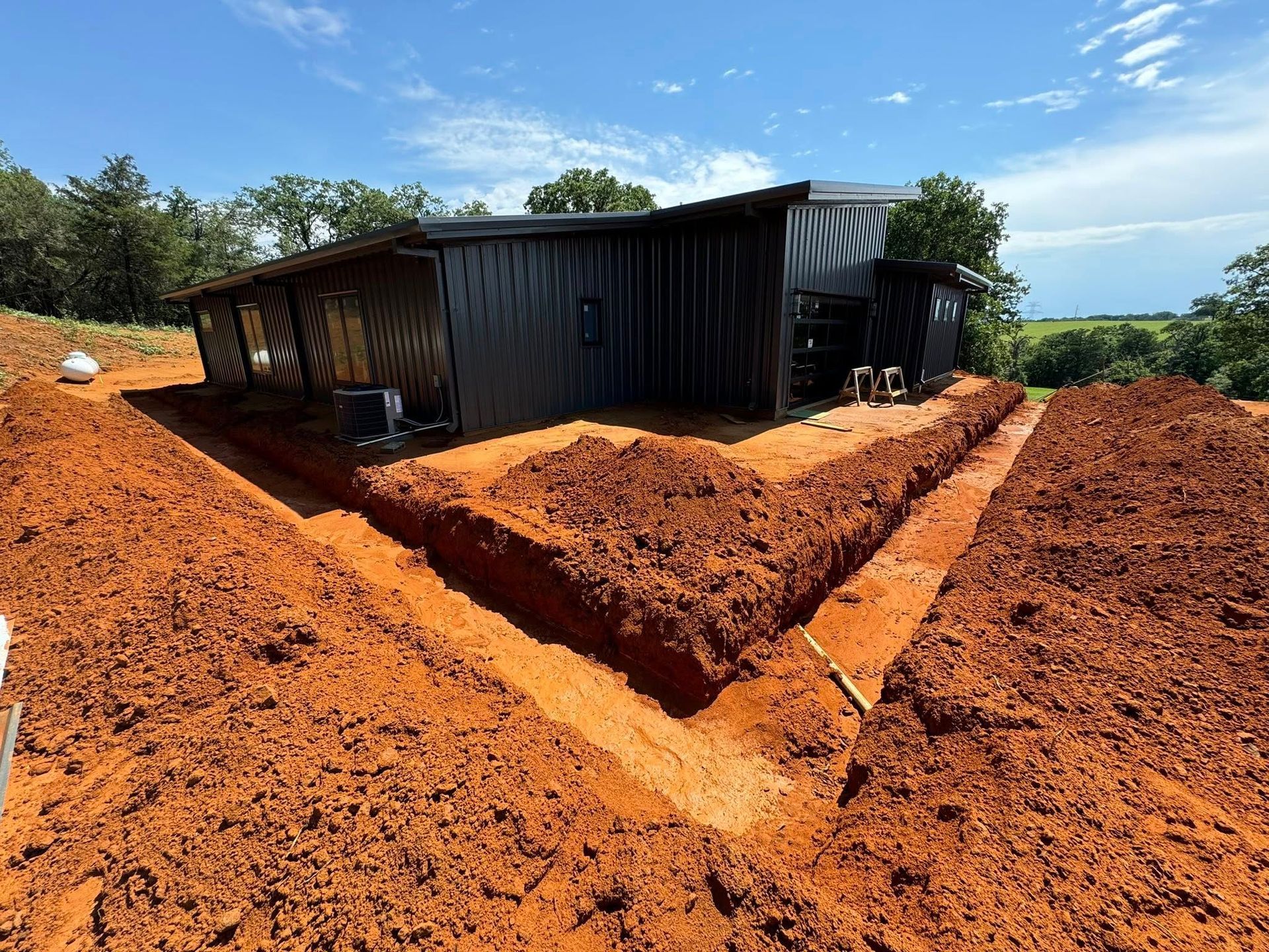 Exterior view of a building with trenches dug in the red earth for a foundation.