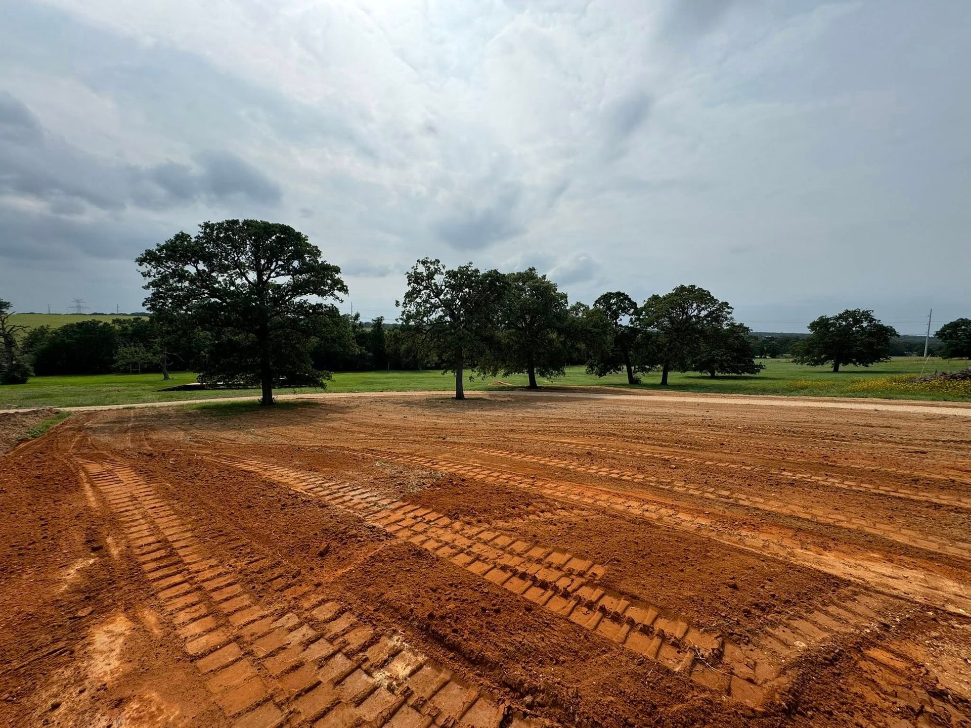 A plowed field with tire tracks in front of trees under a cloudy sky.