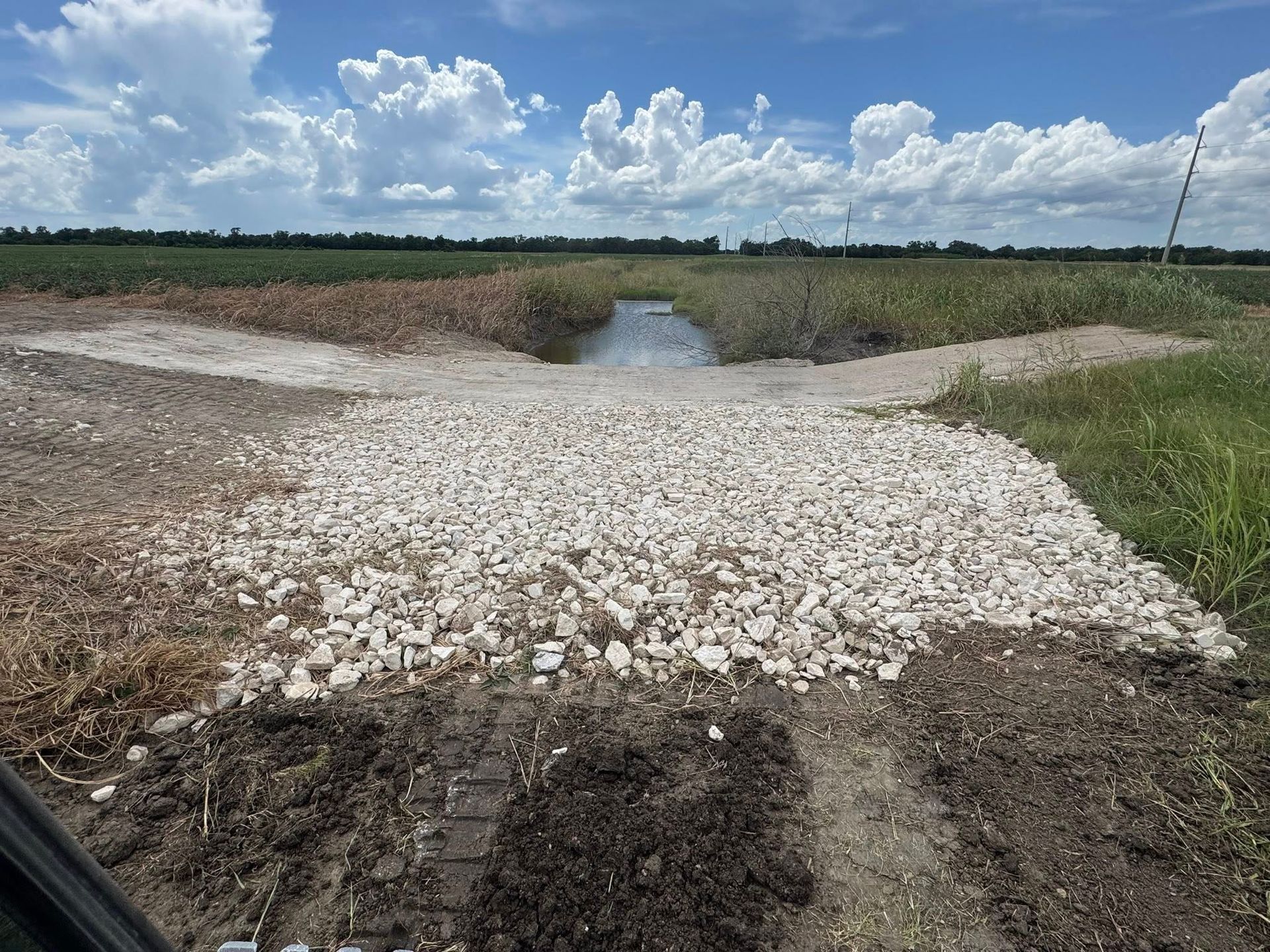 Gravel road leading to a water channel in an agricultural field under a cloudy sky.