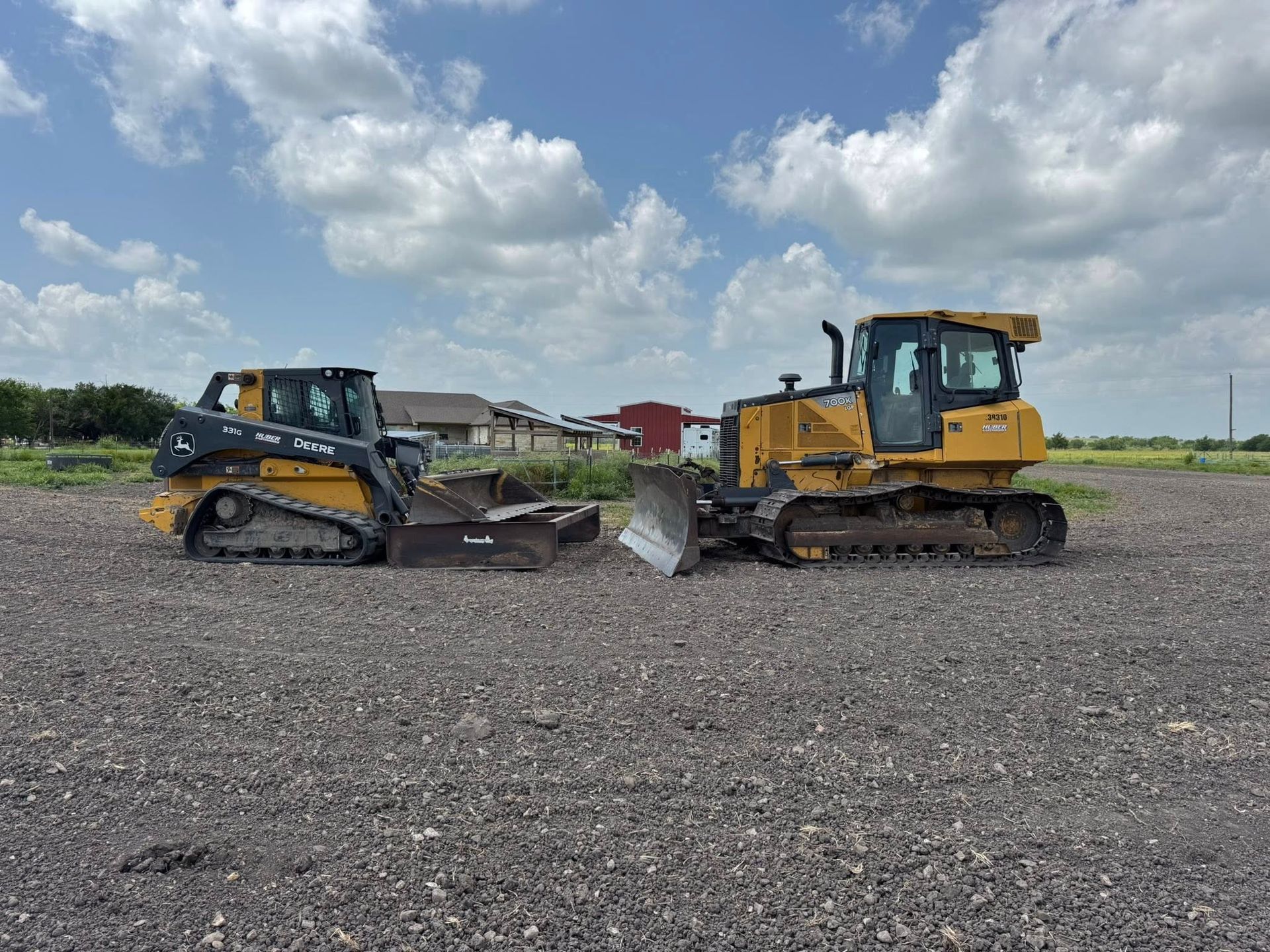Two yellow construction vehicles, a skid steer and a bulldozer, parked on gravel under a cloudy sky.