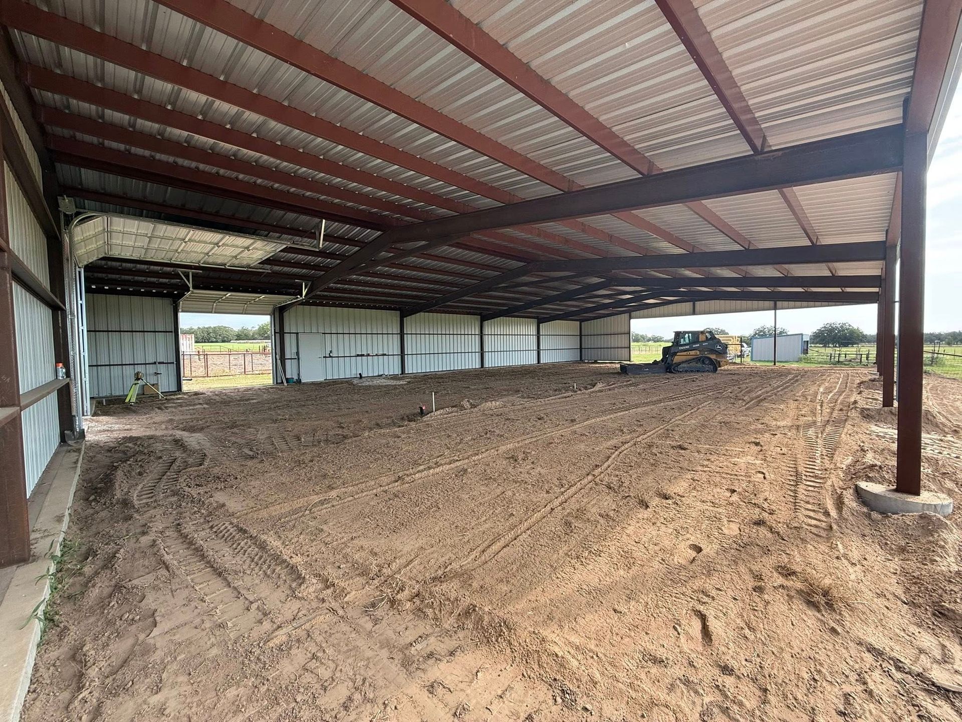 A large open metal barn with dirt floor; a tractor is inside.