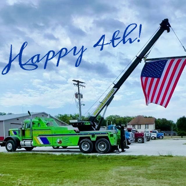 A green tow truck with an american flag and the words happy 4th