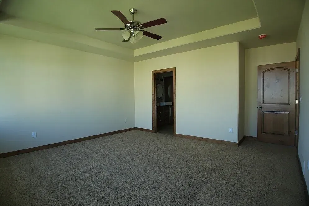 An empty bedroom with a ceiling fan and a door leading to a bathroom.