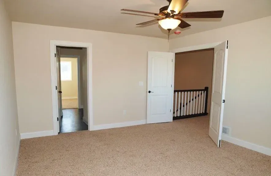 An empty bedroom with a ceiling fan and a staircase.