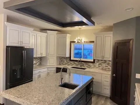 A kitchen with white cabinets , granite counter tops , black appliances and a large island.