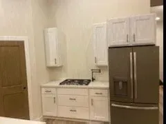 A kitchen with white cabinets, a stove, a refrigerator, and a sink.