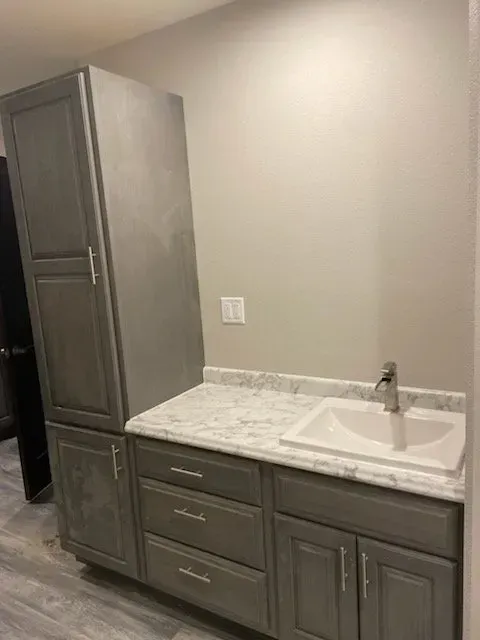 A bathroom with a sink , cabinets , and a marble counter top.