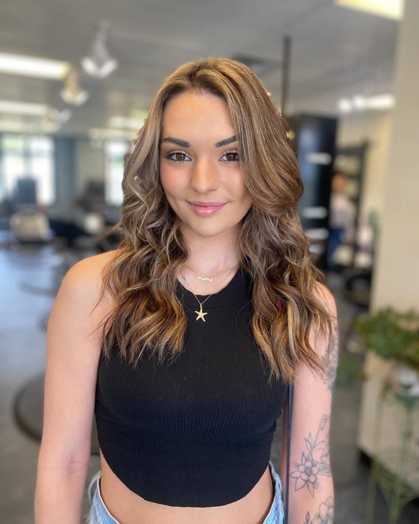 A woman wearing a black crop top and jeans is standing in a salon.