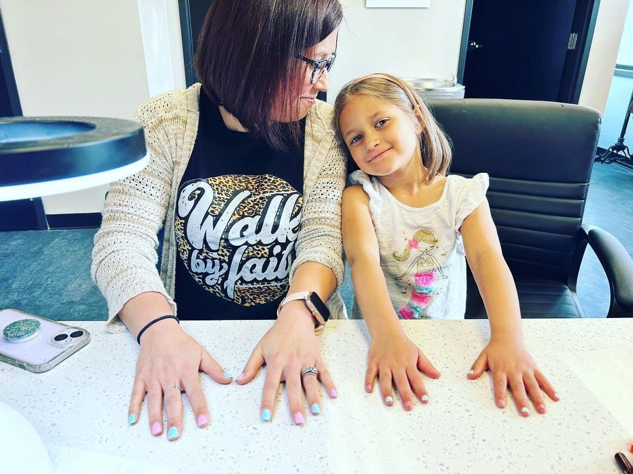 A woman and a little girl are sitting at a table with their hands on the table.