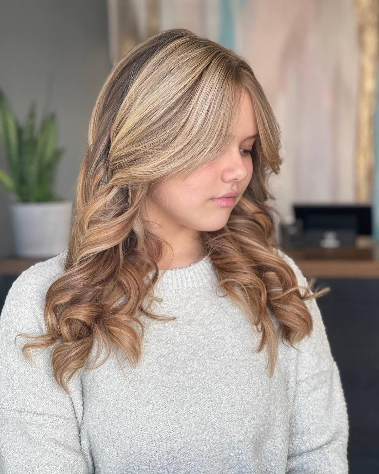 A young woman with long blonde hair is wearing a grey sweater.