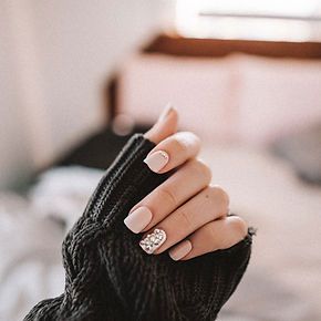 A woman is wearing a black sweater and holding her hand up with her nails painted pink.