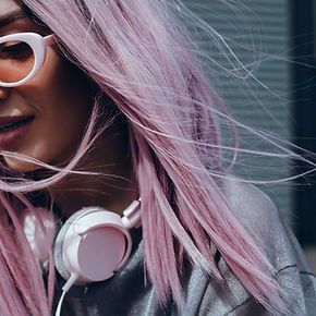 A woman with pink hair is wearing headphones and glasses.