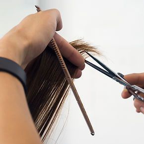 A woman is getting her hair cut by a hairdresser with scissors.