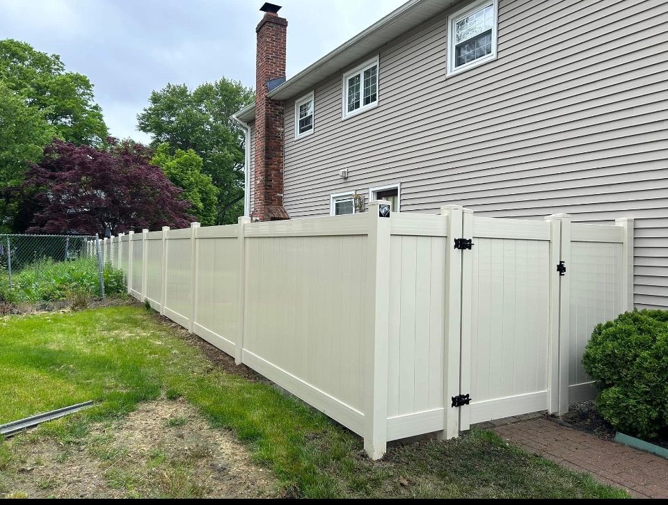 Tan Vinyl fence attached to house.  Trees in the background.