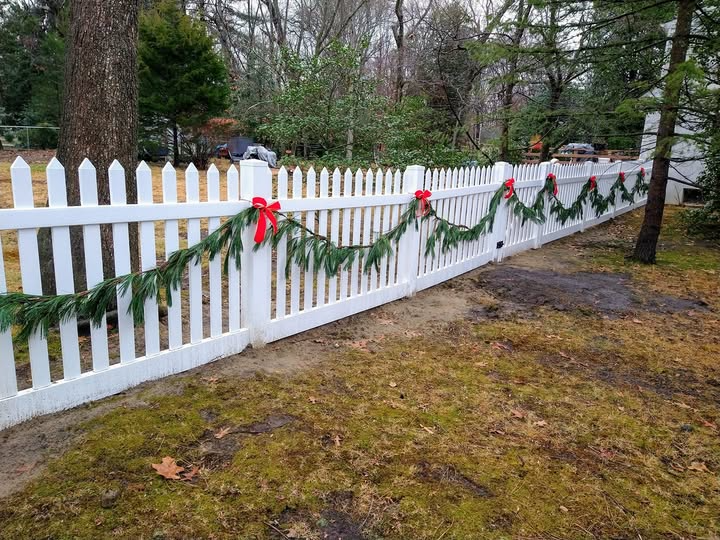 White picket fence decorated with garland and red bows for the holidays.