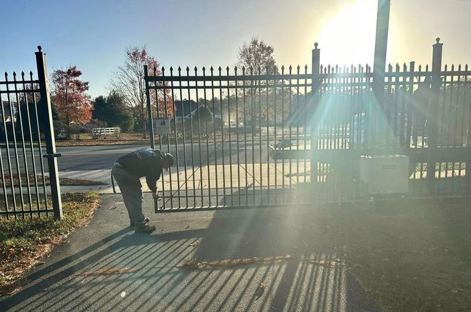 Black metal fence surrounding a pool and yard, with trees in the background.