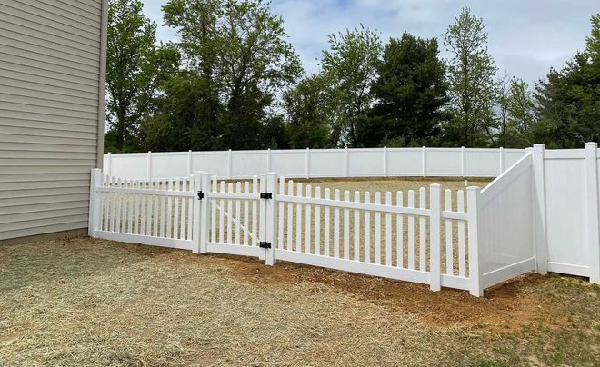 Black chain-link fence encloses a grassy area. A truck with open doors is behind the fence with a sign. Trees in the background.