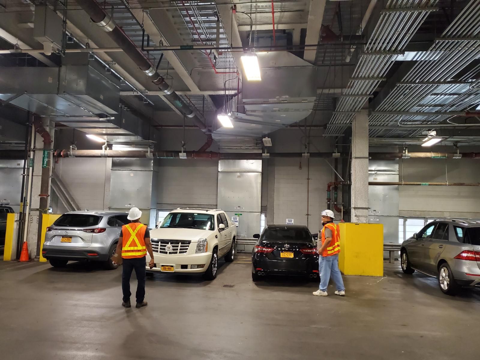 Two men are standing in a parking garage with cars parked in it