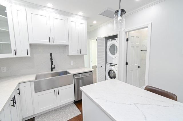 A kitchen with white cabinets , a sink , a dishwasher , and a washer and dryer.