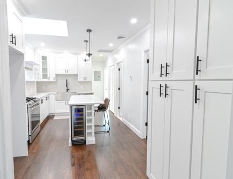 A kitchen with white cabinets , stainless steel appliances , and a wine cooler.