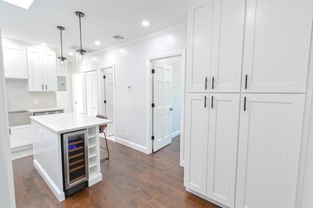 A kitchen with white cabinets and a wine cooler on the island.