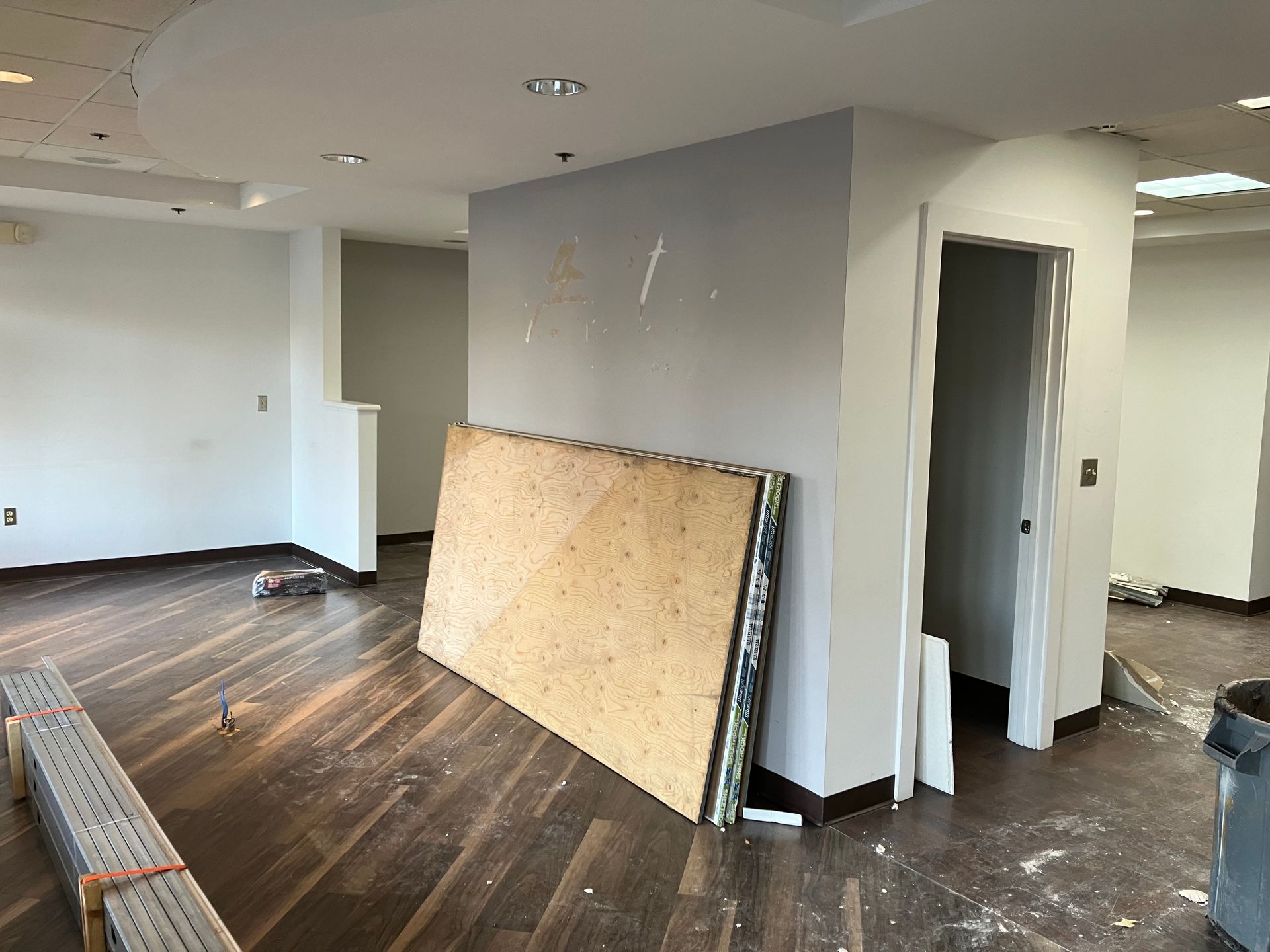 An empty room with a wooden floor and a large piece of plywood on the floor.