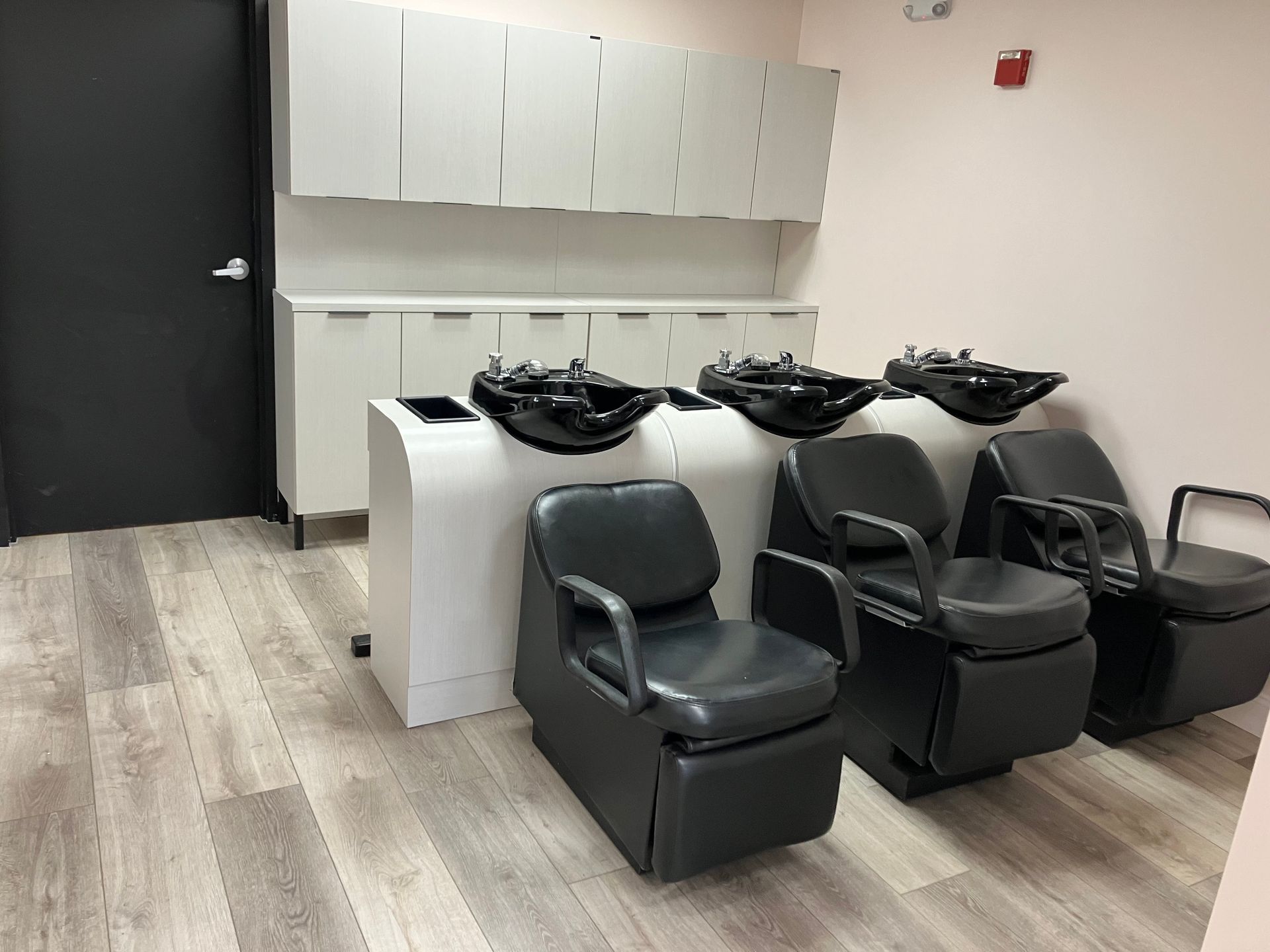 A row of hair salon chairs with sinks in a room.