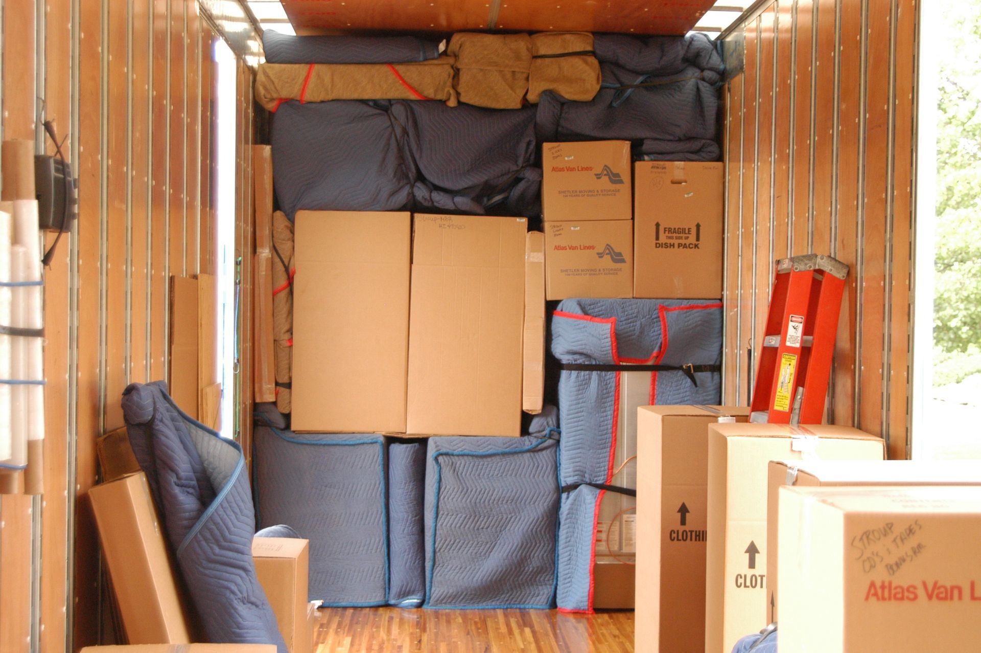 Inside of a packed moving truck, filled with boxes and wrapped furniture.