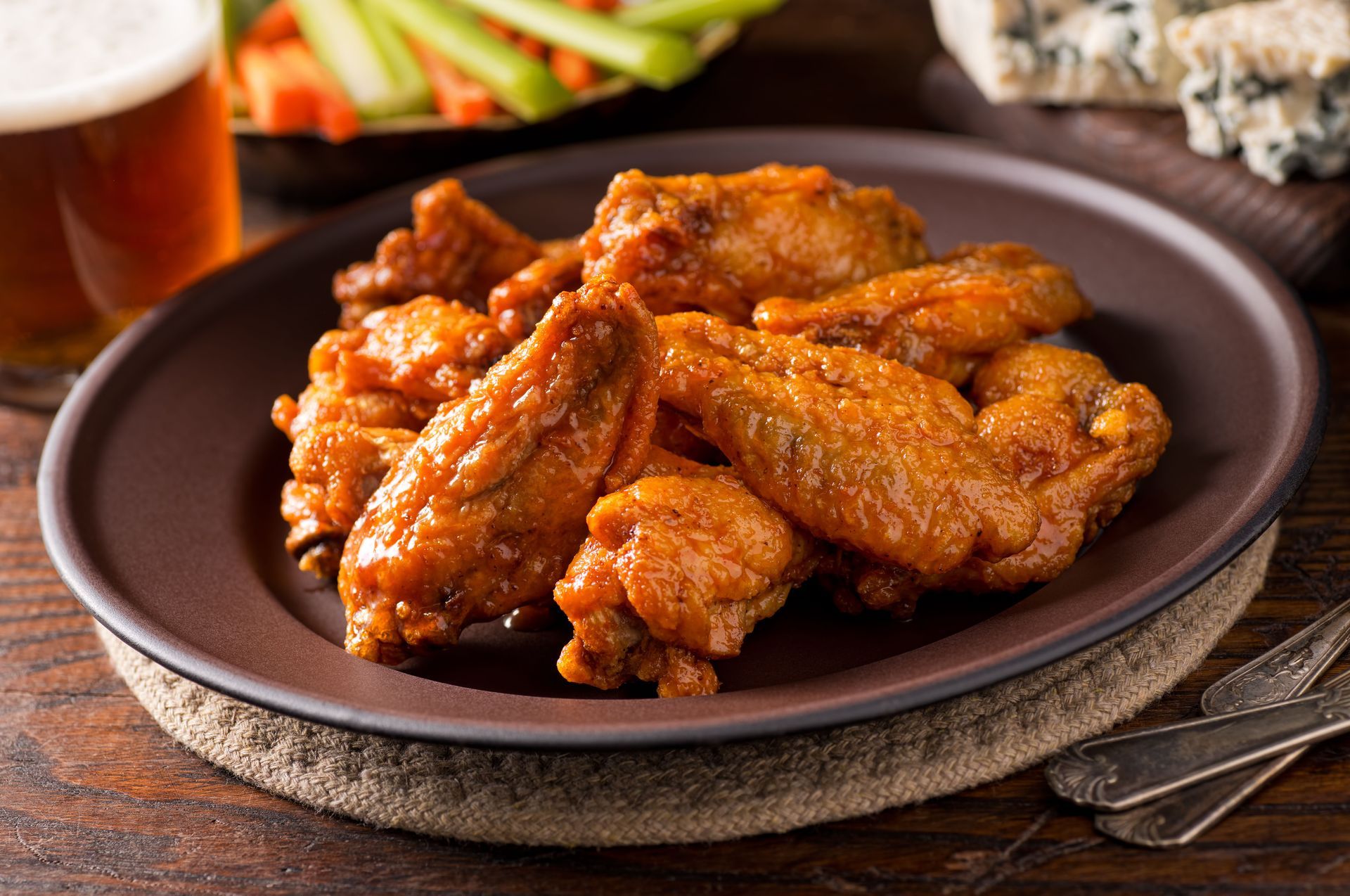 Plate of saucy chicken wings on a rustic table, with celery sticks in the background