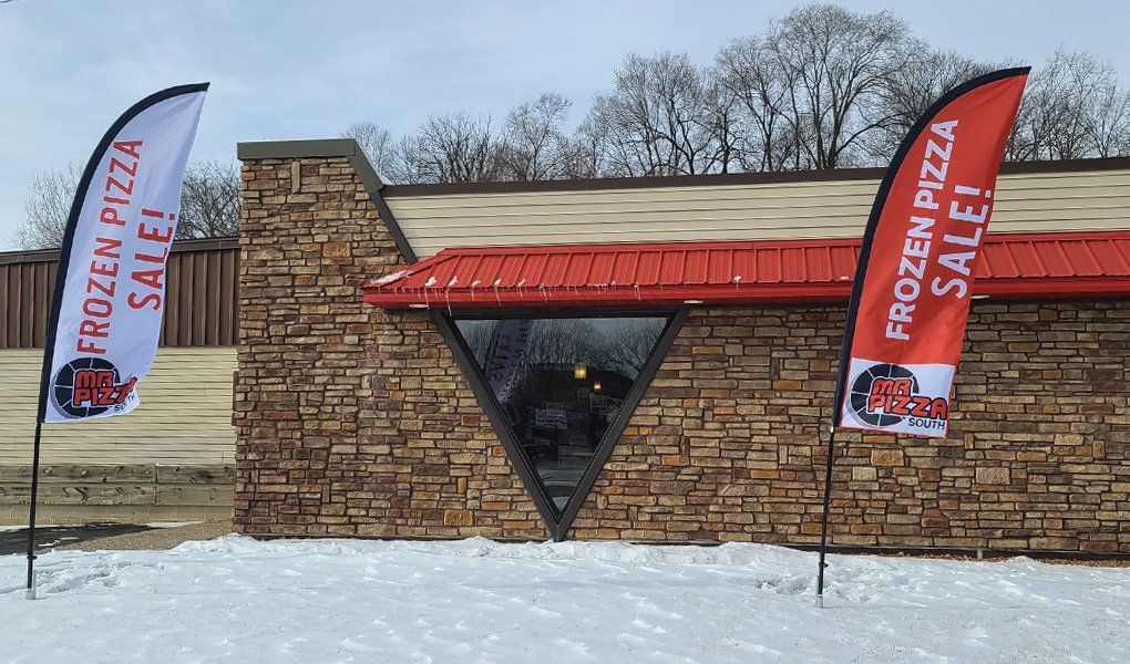 Stone roadside pizza kiosk in snowy field with two Frozen Pizza Sale flags