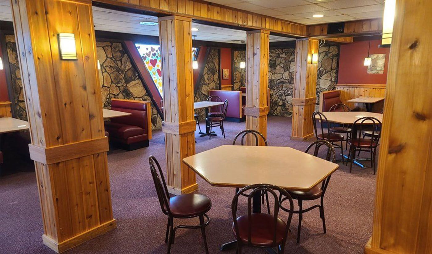 Cozy lodge lounge with wood paneling, tables, chairs, and warm lighting