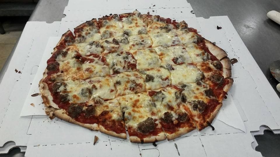 A large cheese pizza on a white cardboard box, with a browned crust and scattered toppings.