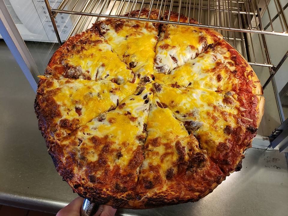 Large cheese pizza on a metal rack, with browned crust and sliced wedges.
