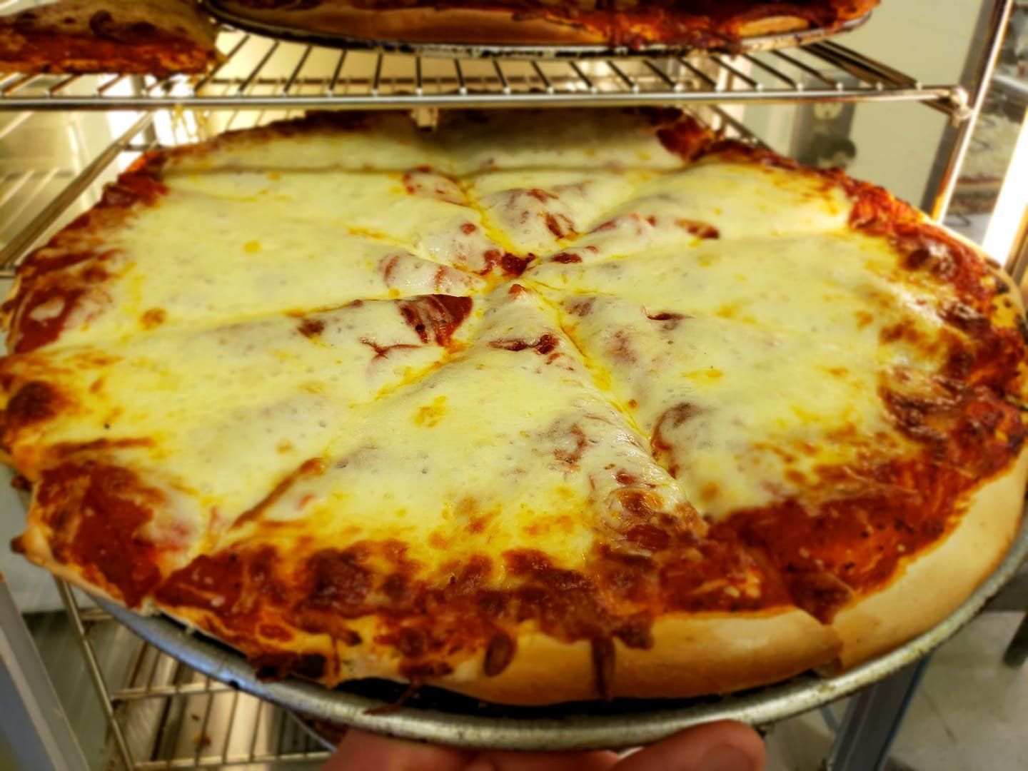Large cheese pizza on a metal rack inside an oven, with browned crust and melted cheese