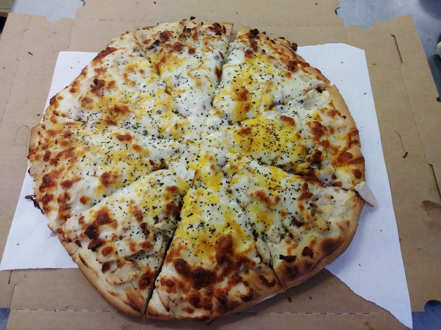 Cheese pizza on a cardboard box, cut into slices, with browned crust and herbs on top