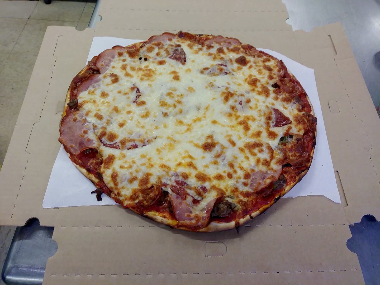 Cheese pizza on a cardboard box, with browned melted cheese and visible crust edges.